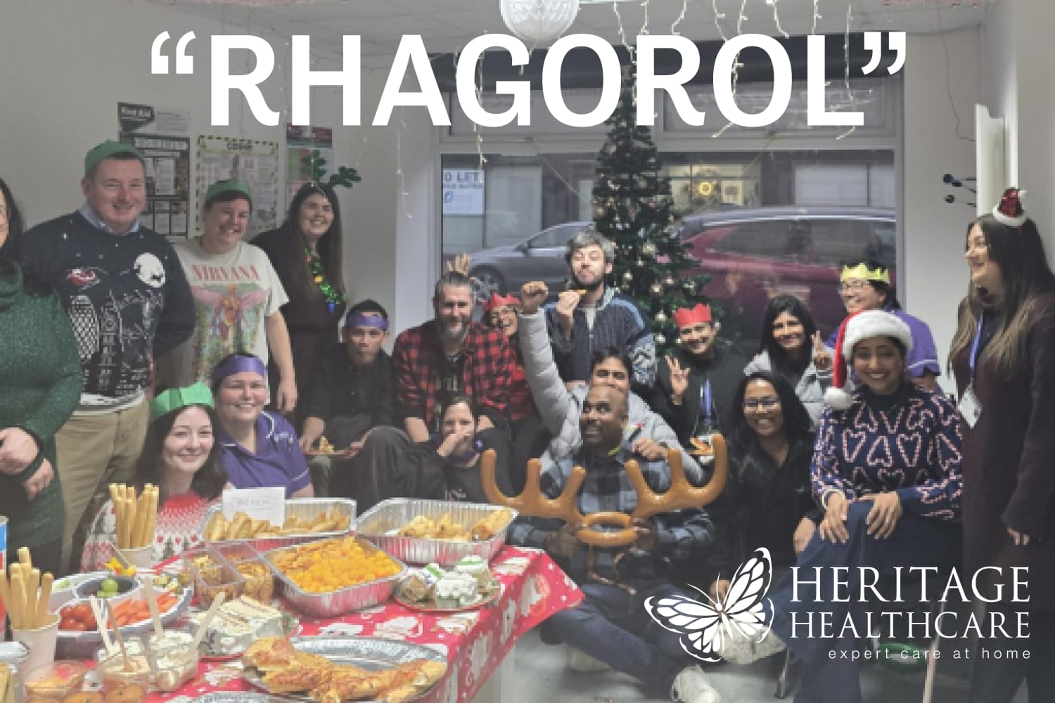 Large group of people celebrating Christmas in front of a Christmas tree and with a large table of food. Image has the caption Rhagorol which is Welsh for Excellent