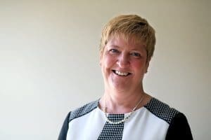 Amanda has short blonde hair and is wearing a black and white outfit with a shell necklace