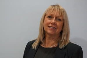 Older blonde lady with with long straight hair and wearing all black with a silver necklace