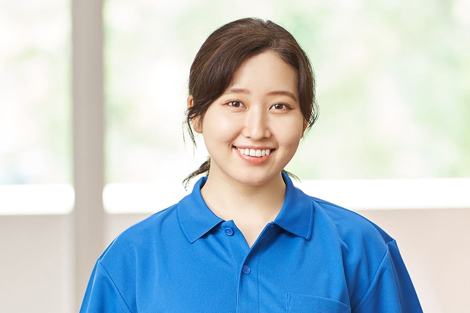 Young female Asian care assistant with dark, tied back hair and wearing a royal blue polo shirt