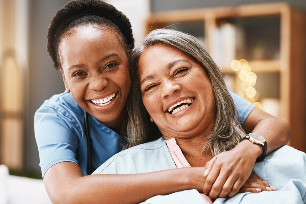 High Quality Home Care Services from Heritage Healthcare Wakefield & Kirklees Black home carer hugs older lady sitting on sofa, both smiling
