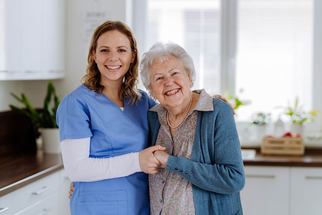 Young nurse hugging her senior woman client. Carer, a white woman with long ginger hair, hugging client, an older white woman with short grey hair.