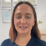 Suzanne is a female with shoulder length light brown hair and pale blue eyes wearing hoop earrings and a blue jumper