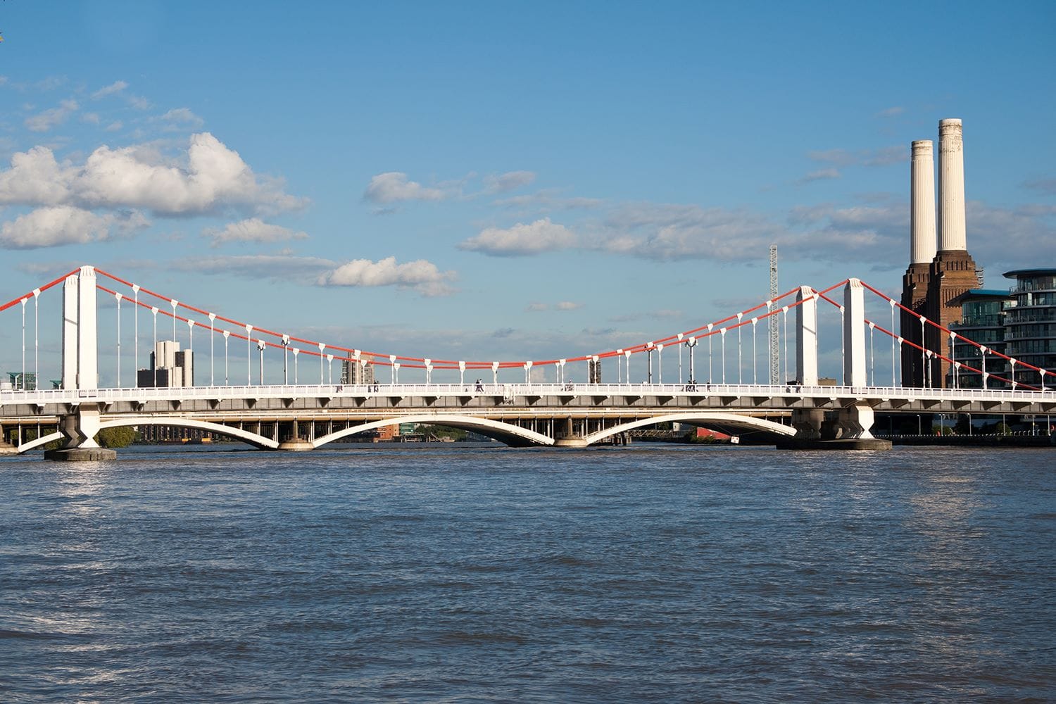 Chelsea Bridge in London. Painted white and red and showing three of the spans across the River Thames with the power station in the background against a sunny blue sky