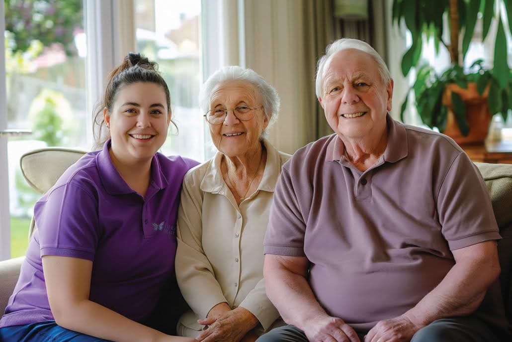 Young female home care assistant with an elderly couple sitting in a living room setting