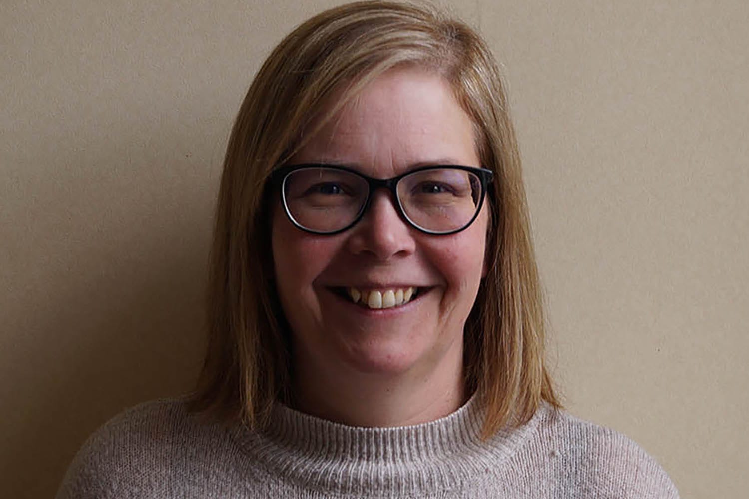 Female with shoulder length light hair wearing glasses and a beige jumper