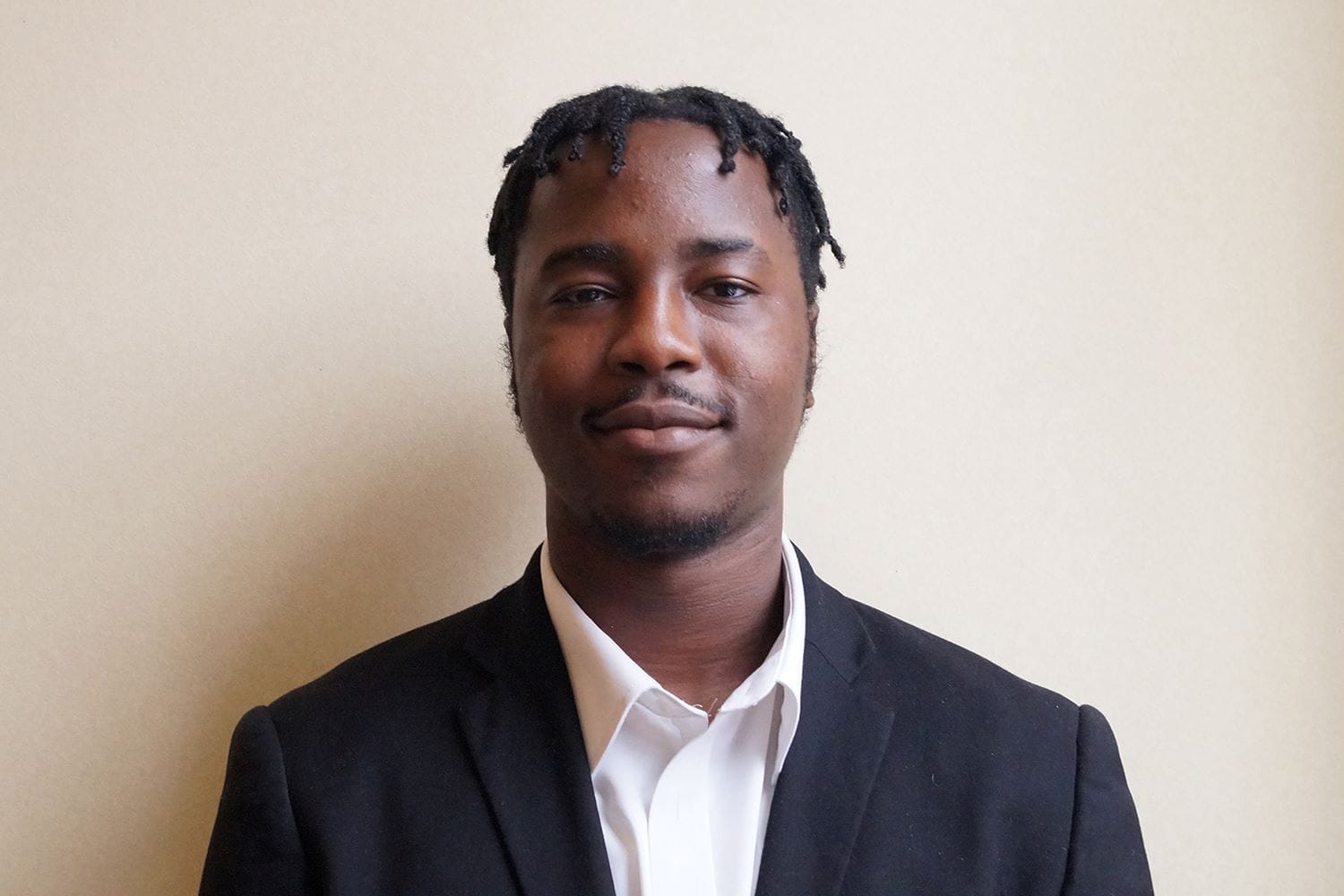 Destiny Oduh - Managing Director - Heritage Healthcare Basildon Young black man with short dreadlocked hair and a small beard wearing a dark business suit and a while shirt