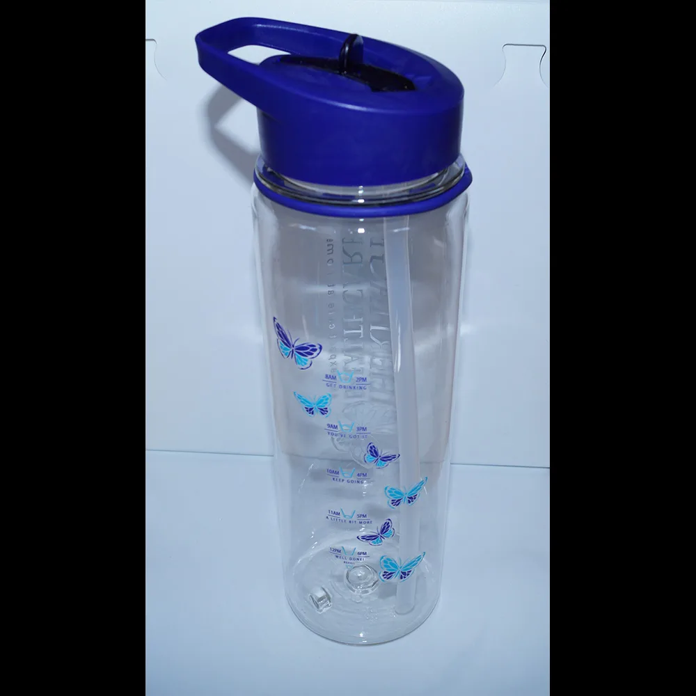 Heritage Healthcare water bottle with time markings, detailing how much water you should have drank by a certain time. The markings start at 8 am and go down to noon before starting at the top from 2 pm till 6 pm. The bottle has a purple top with a purple lid and sipper. The straw inside the cup is see-through.